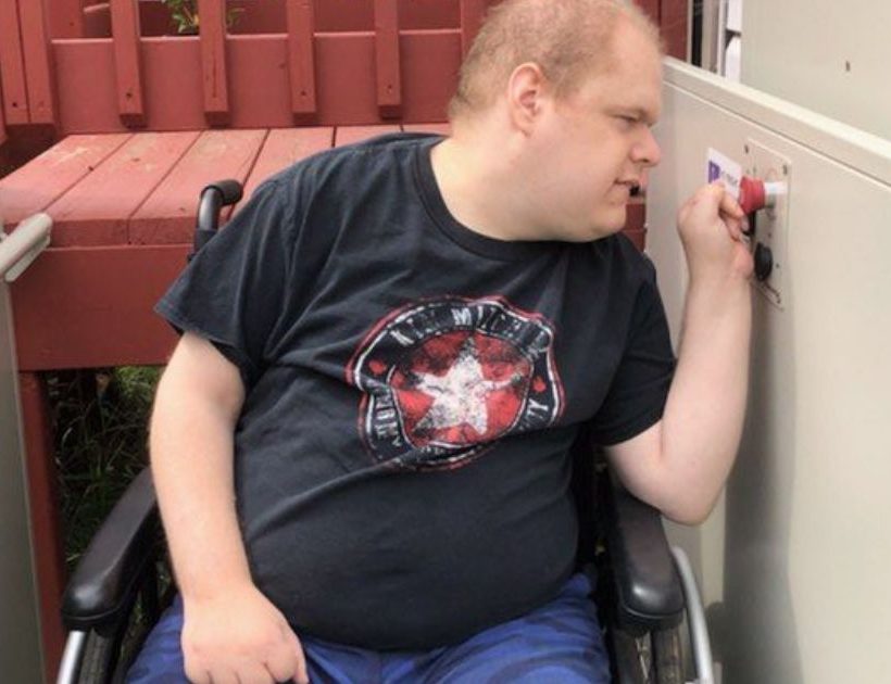 A man in a wheelchair is looking to the left side and pressing a red button.