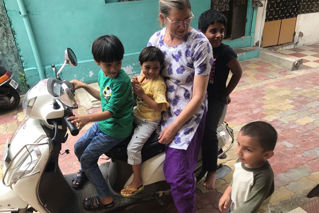 Three kids and an older woman on top of a grey motorcycled, next to a small boy looking to the front