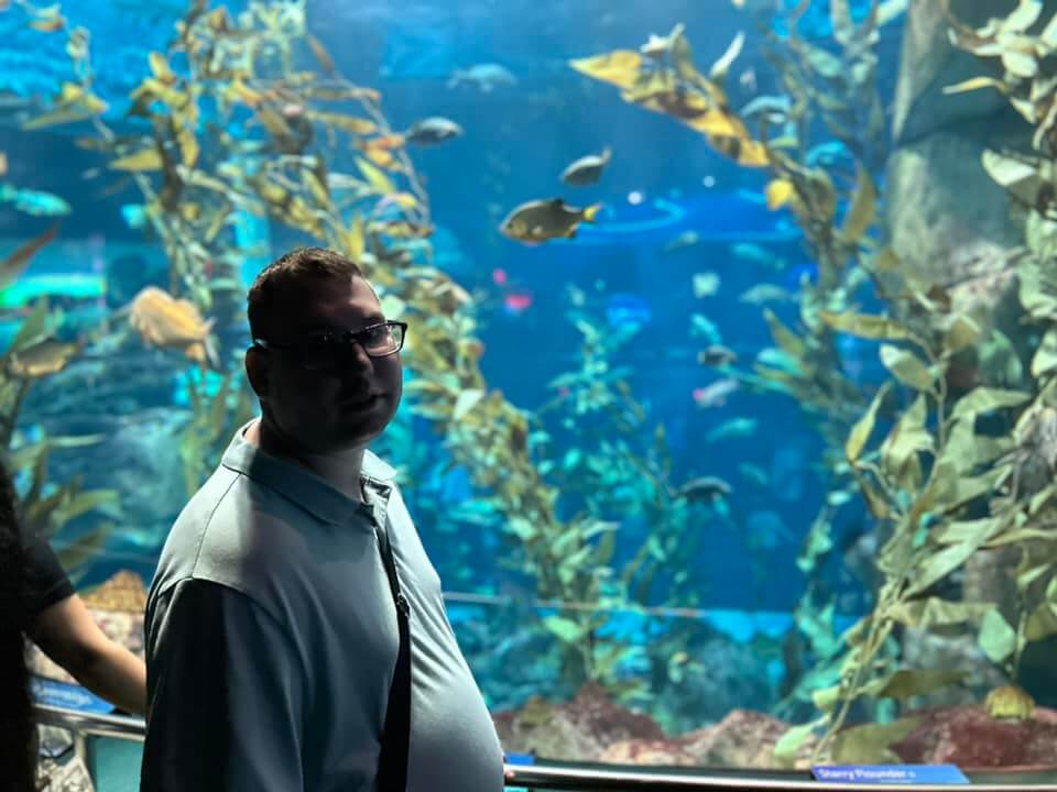 A man is looking at the camera, and behind him, there is an aquarium.
