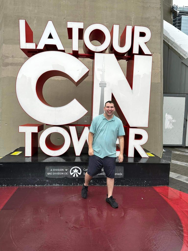 A man is smiling at the camera, and behind him, there is a "LA TOUR CV TOWER" sign.